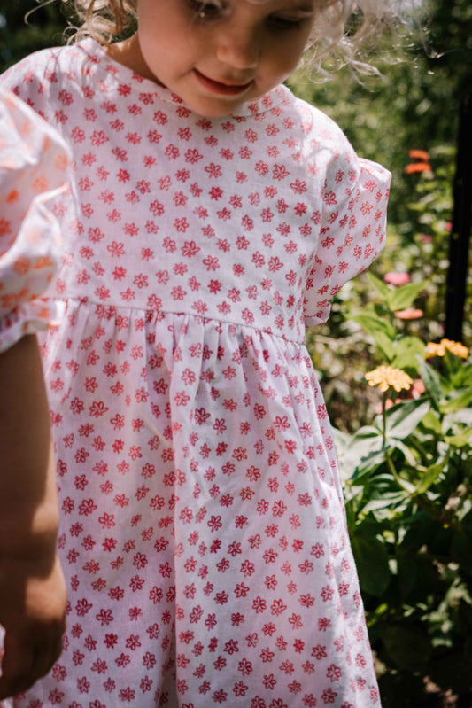 kids smock style dress in pink and white flower floral print with puff sleeves and adjustable back made from a cotton linen blend fabric thats soft