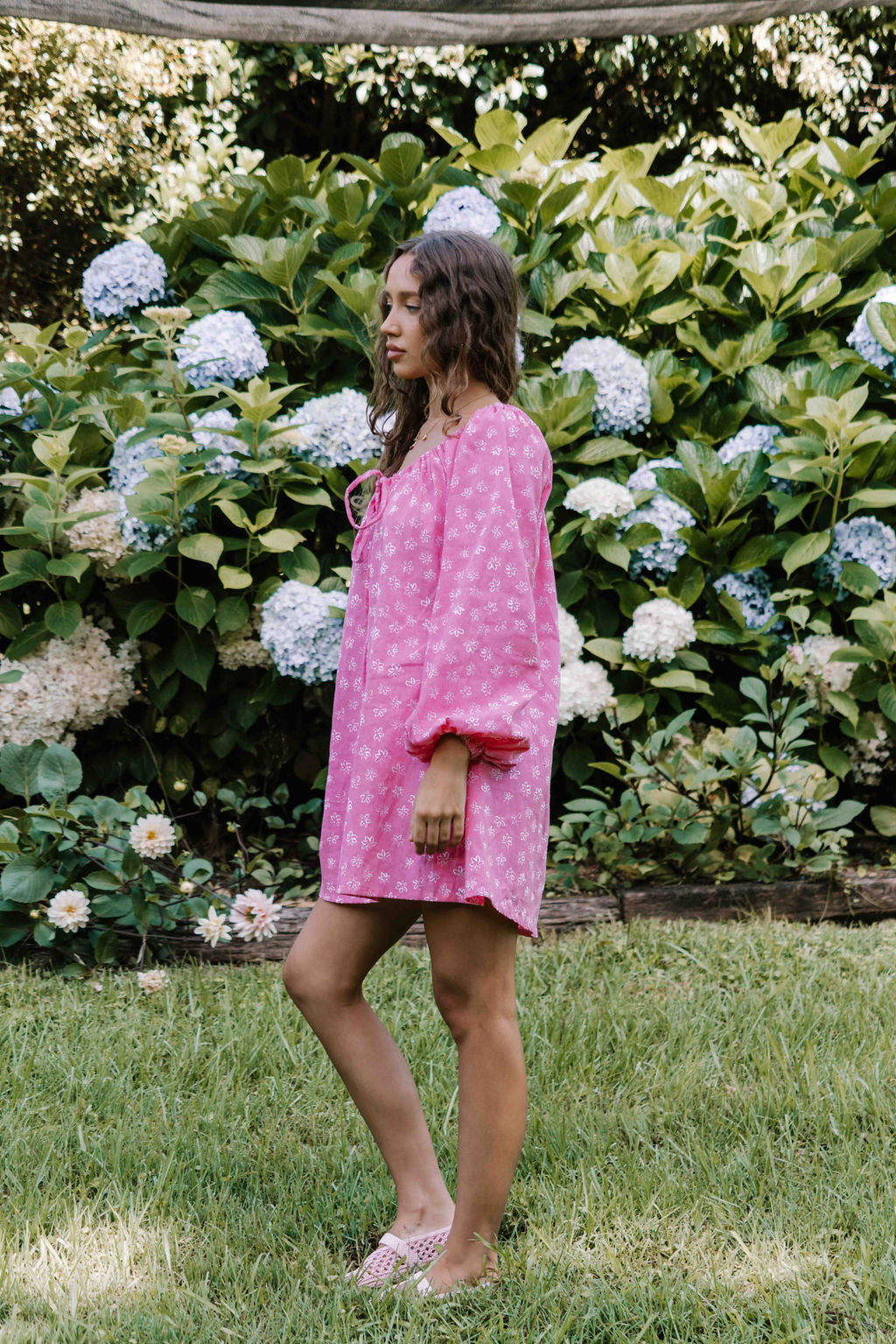 drawstring neckline shift mini dress with a statement balloon long sleeve with elastic wrists, rounded neckline with adjustable bow tie at the front. Hand painted white flower print on a bright candy pink cotton linen fabric.