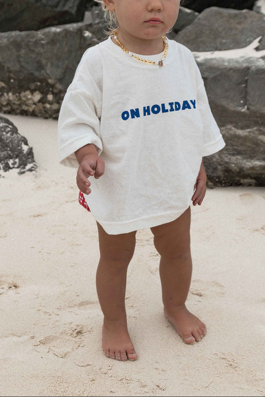 Children's t-shirt made from soft 100% orgaic cotton in a off white oversized fit with blue ‘ON HOLIDAY’ graphic. The shirt has a relaxed, comfy fit.