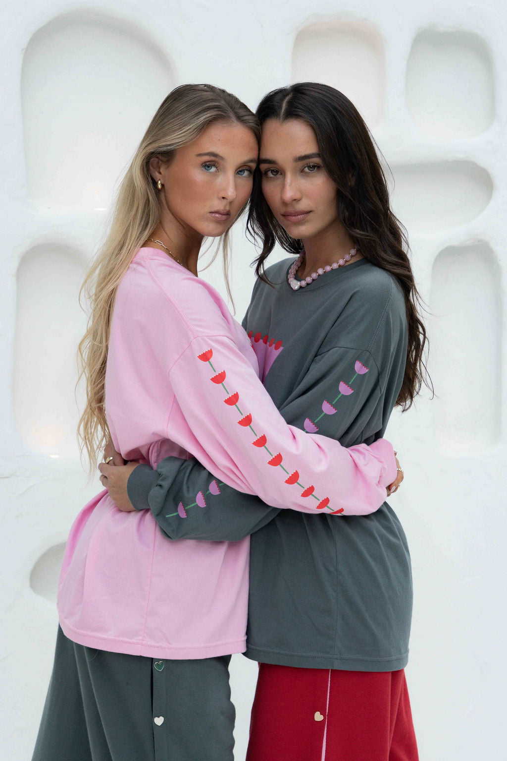 Women’s oversized long-sleeve t-shirt in baby pink, featuring belle sleeves gathered into chunky cuffs. Designed in ultra-soft 100% organic cotton, it showcases a bold flower graphic in pink, red, and green on the front and repeated down each sleeve, with a small 'häll' logo detail.