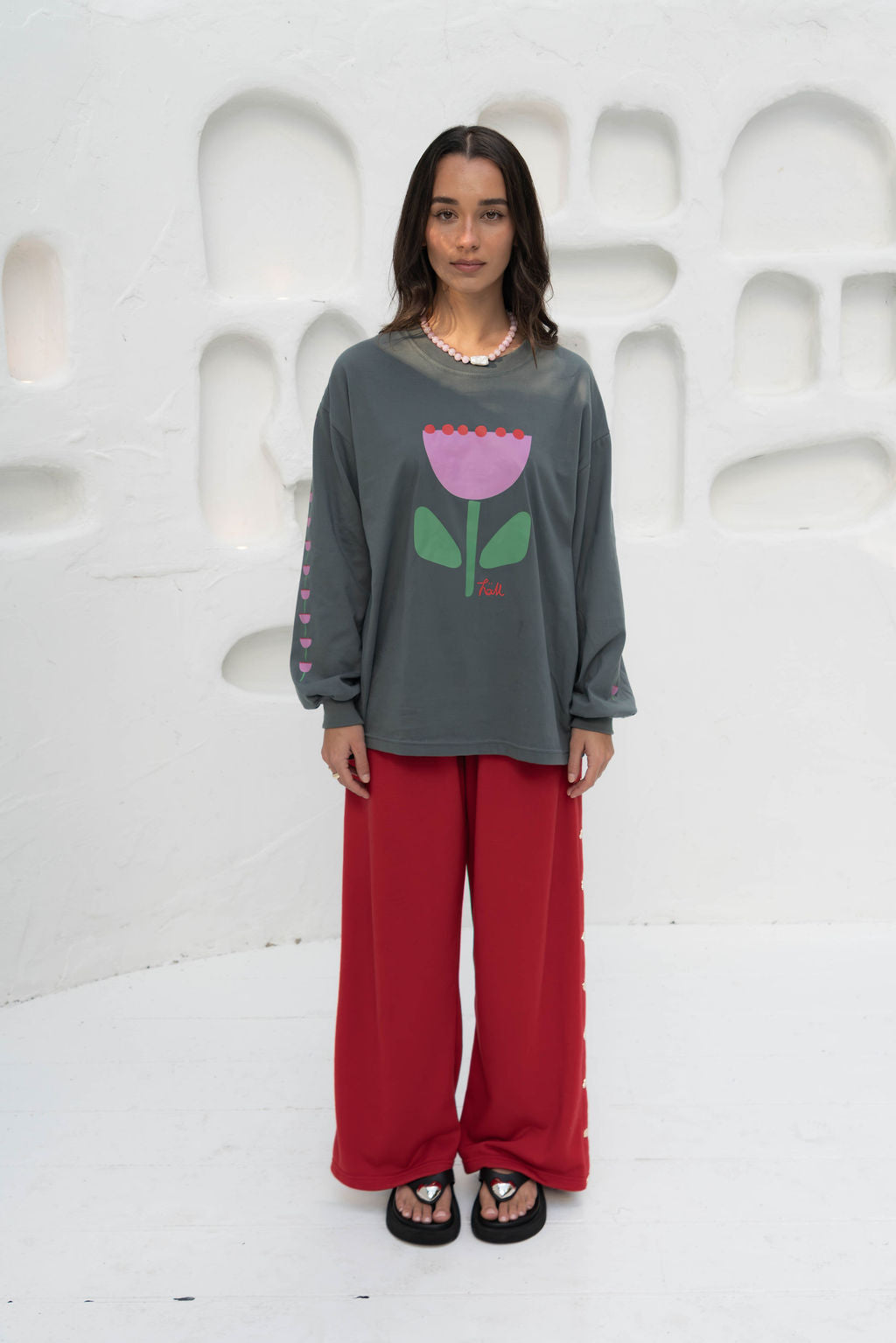 Women’s oversized long-sleeve t-shirt in charcoal, featuring belle sleeves gathered into chunky cuffs. Designed in ultra-soft 100% organic cotton, it showcases a bold flower graphic in pink, red, and green on the front and repeated down each sleeve, with a small 'häll' logo detail.