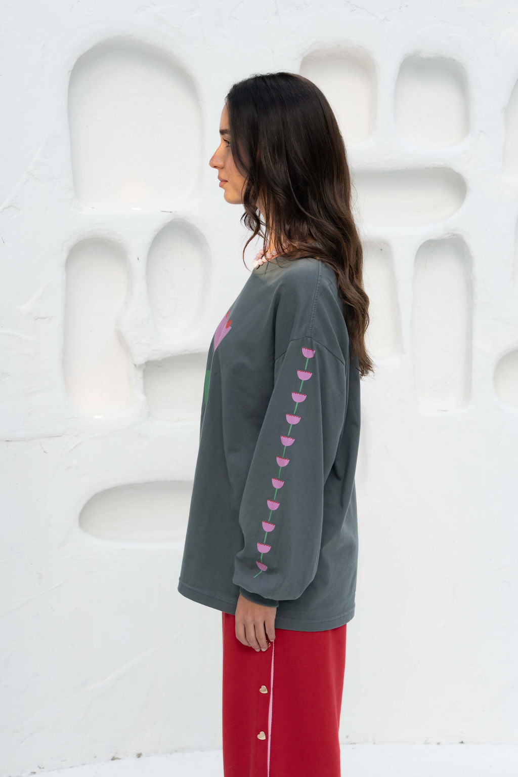 Women’s oversized long-sleeve t-shirt in charcoal, featuring belle sleeves gathered into chunky cuffs. Designed in ultra-soft 100% organic cotton, it showcases a bold flower graphic in pink, red, and green on the front and repeated down each sleeve, with a small 'häll' logo detail.