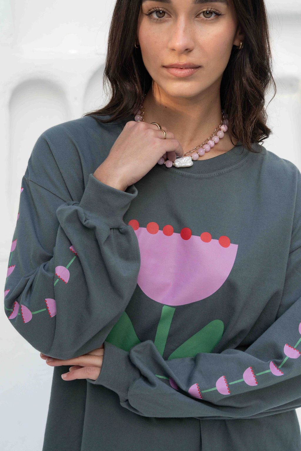 Women’s oversized long-sleeve t-shirt in charcoal, featuring belle sleeves gathered into chunky cuffs. Designed in ultra-soft 100% organic cotton, it showcases a bold flower graphic in pink, red, and green on the front and repeated down each sleeve, with a small 'häll' logo detail.