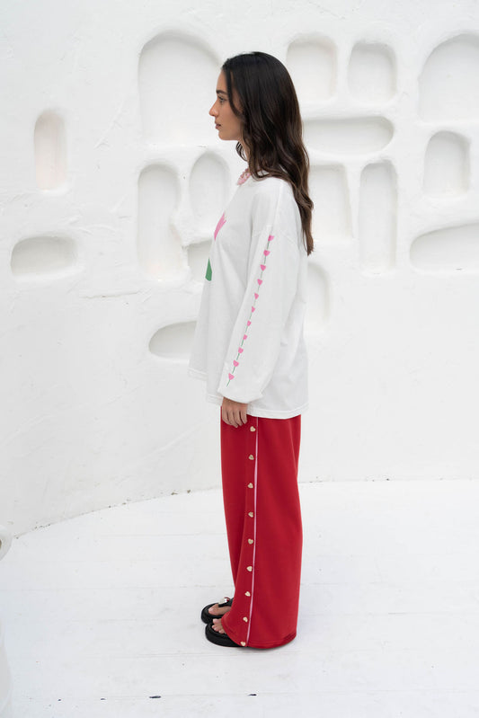 Women’s oversized long-sleeve t-shirt in white, featuring belle sleeves gathered into chunky cuffs. Designed in ultra-soft 100% organic cotton, it showcases a bold flower graphic in pink and green on the front and repeated down each sleeve, with a small 'häll' logo detail.