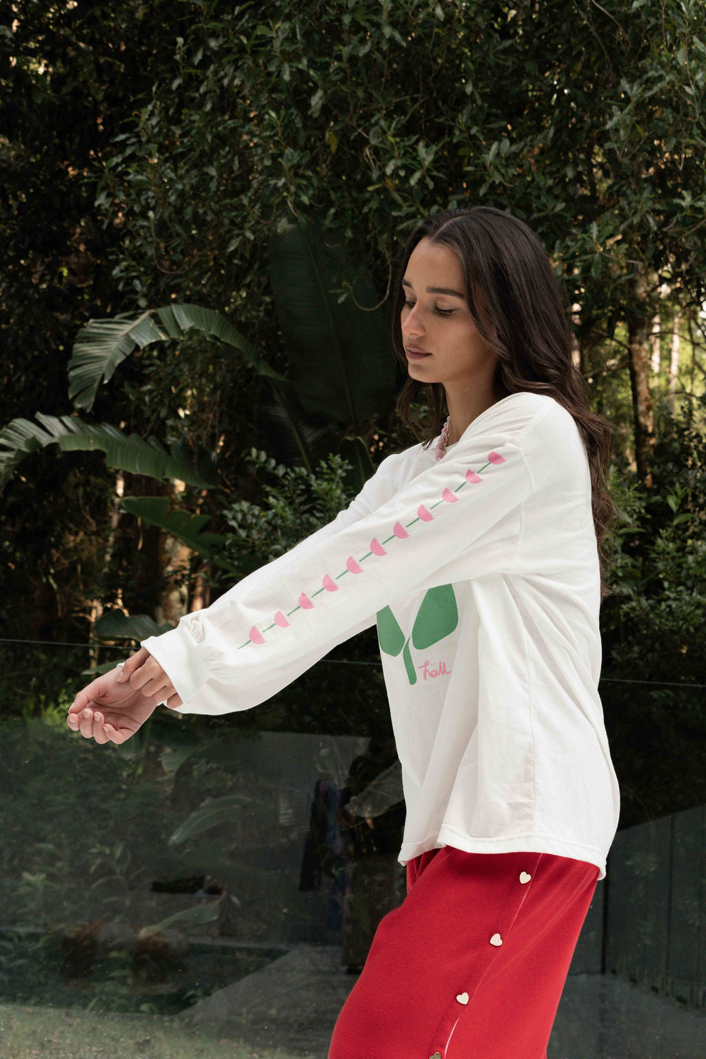 Women’s oversized long-sleeve t-shirt in white, featuring belle sleeves gathered into chunky cuffs. Designed in ultra-soft 100% organic cotton, it showcases a bold flower graphic in pink and green on the front and repeated down each sleeve, with a small 'häll' logo detail.