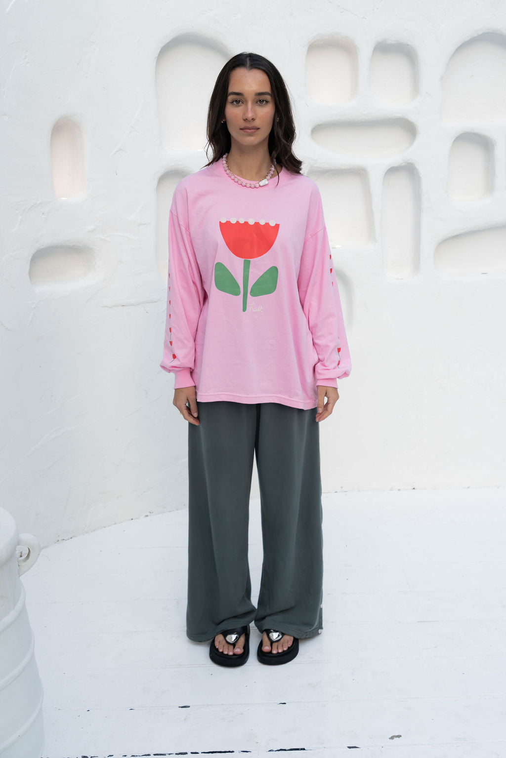 Women’s oversized long-sleeve t-shirt in baby pink, featuring belle sleeves gathered into chunky cuffs. Designed in ultra-soft 100% organic cotton, it showcases a bold flower graphic in pink, red, and green on the front and repeated down each sleeve, with a small 'häll' logo detail.