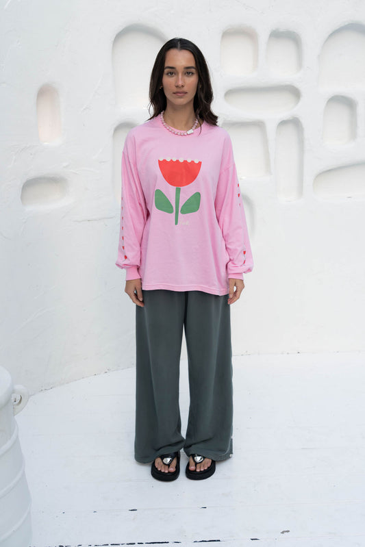 Women’s oversized long-sleeve t-shirt in baby pink, featuring belle sleeves gathered into chunky cuffs. Designed in ultra-soft 100% organic cotton, it showcases a bold flower graphic in pink, red, and green on the front and repeated down each sleeve, with a small 'häll' logo detail.