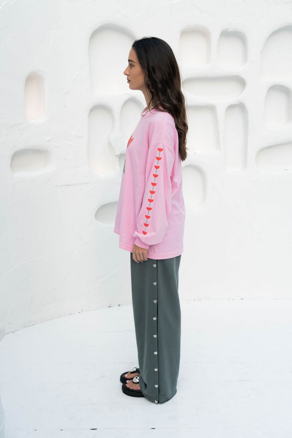 Women’s oversized long-sleeve t-shirt in baby pink, featuring belle sleeves gathered into chunky cuffs. Designed in ultra-soft 100% organic cotton, it showcases a bold flower graphic in pink, red, and green on the front and repeated down each sleeve, with a small 'häll' logo detail.