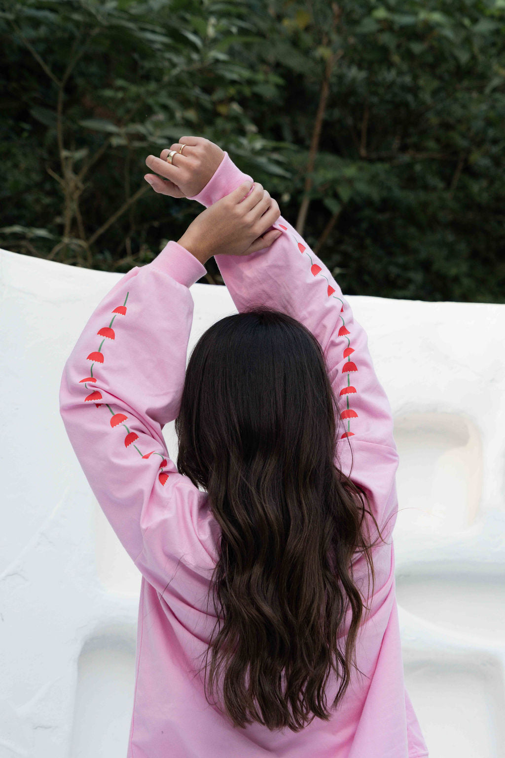 Women’s oversized long-sleeve t-shirt in baby pink, featuring belle sleeves gathered into chunky cuffs. Designed in ultra-soft 100% organic cotton, it showcases a bold flower graphic in pink, red, and green on the front and repeated down each sleeve, with a small 'häll' logo detail.