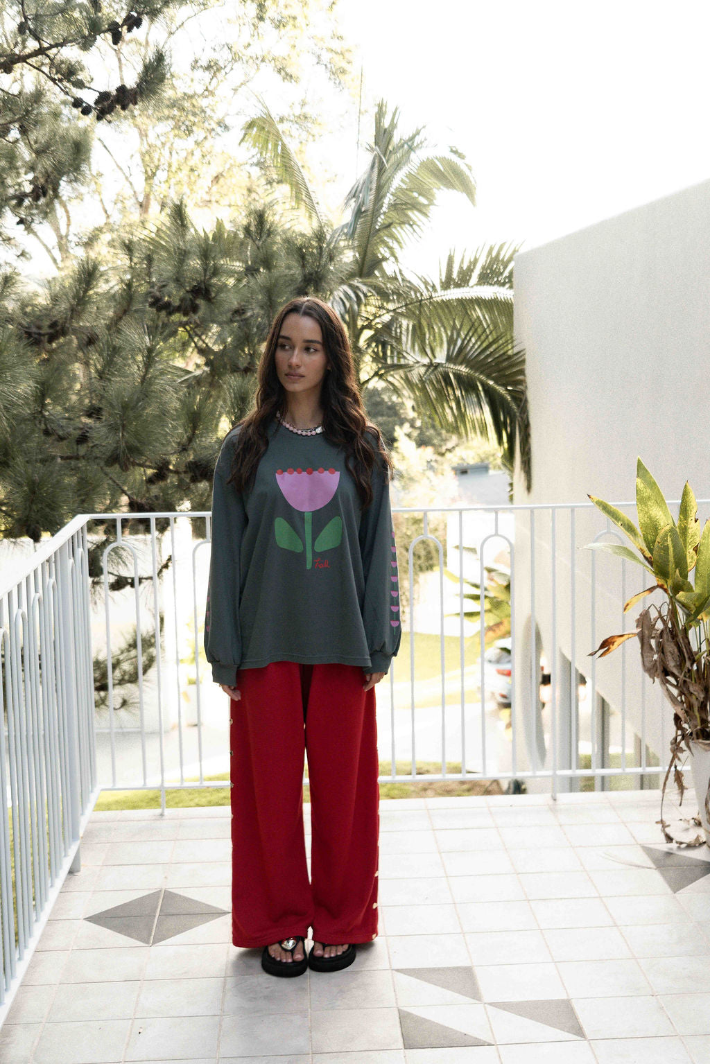 Women’s oversized long-sleeve t-shirt in charcoal, featuring belle sleeves gathered into chunky cuffs. Designed in ultra-soft 100% organic cotton, it showcases a bold flower graphic in pink, red, and green on the front and repeated down each sleeve, with a small 'häll' logo detail.