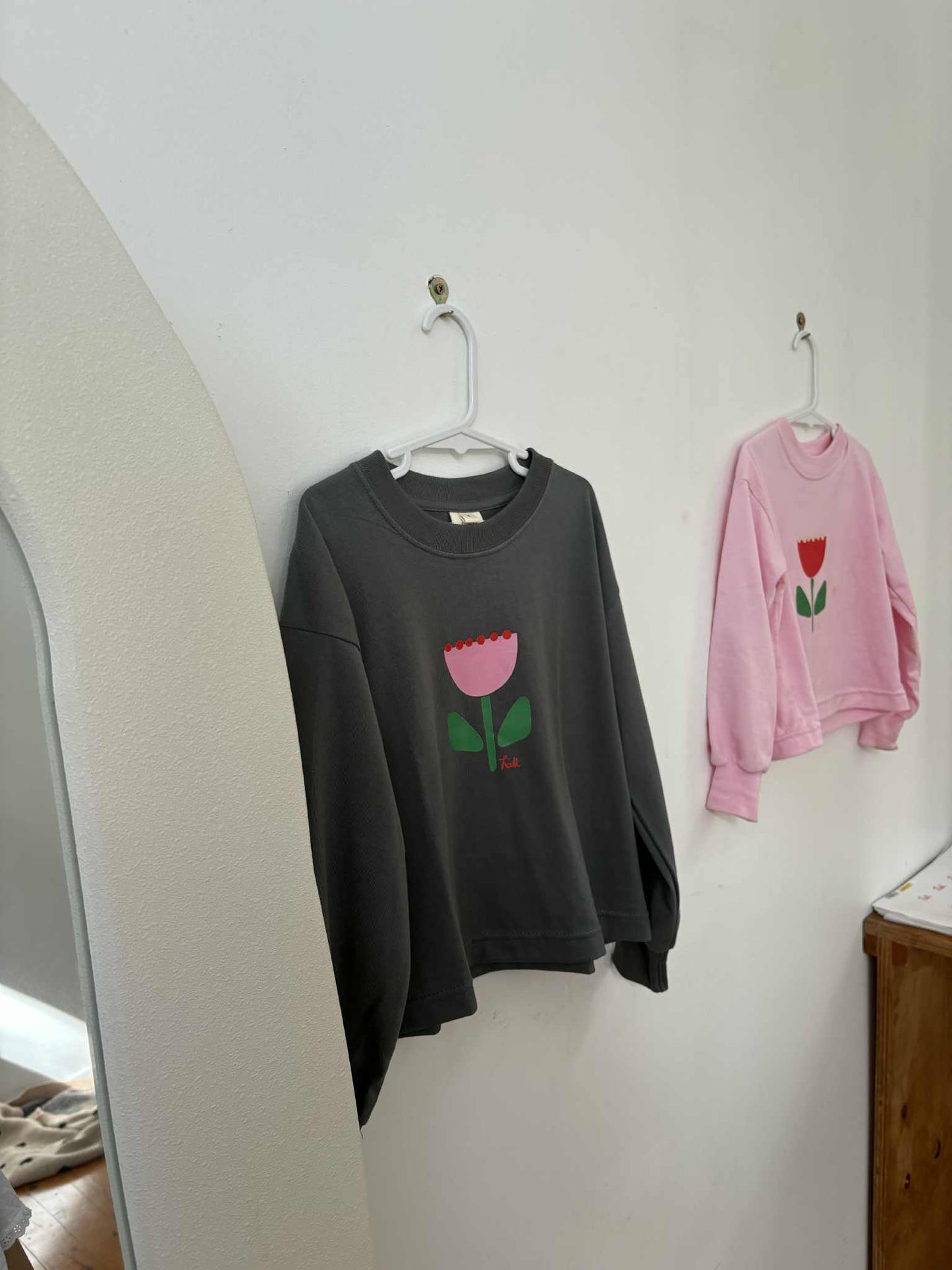 kids long sleeve tshirt featuring a belle sleeve with chunky cuffs detail oversized fit with bold pink green and red flower graphic hand painted logo in white on a charcoal organic cotton tshirt comfortable boxxy fit soft fabric made for playing fun and adventure