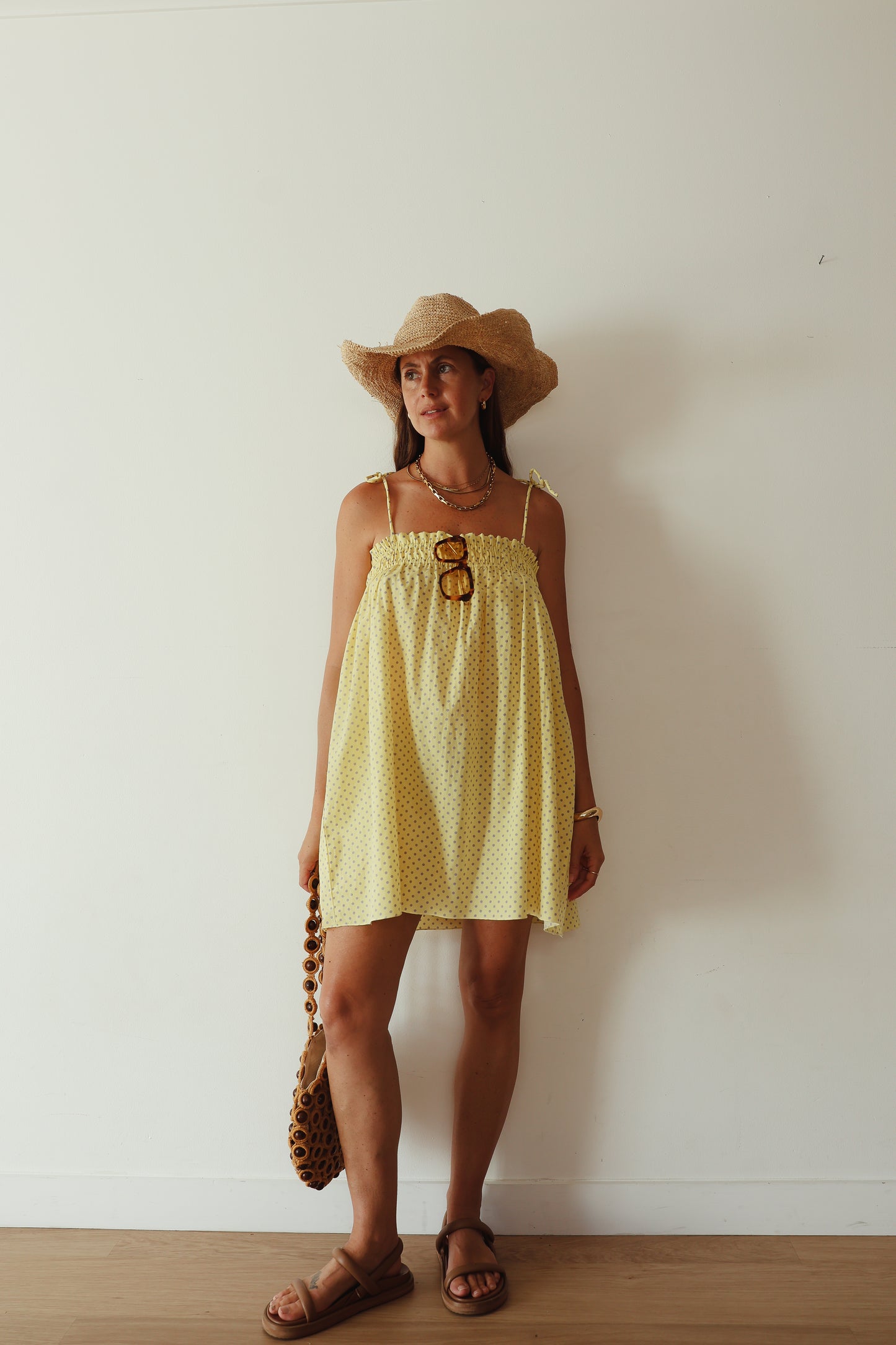 A yellow mini smock dress with a ruched bust and adjustable spagetti shoulder straps that tie. The fabric is a light weight 100% soft cotton in butter yelllow with purple lilac polkadots.