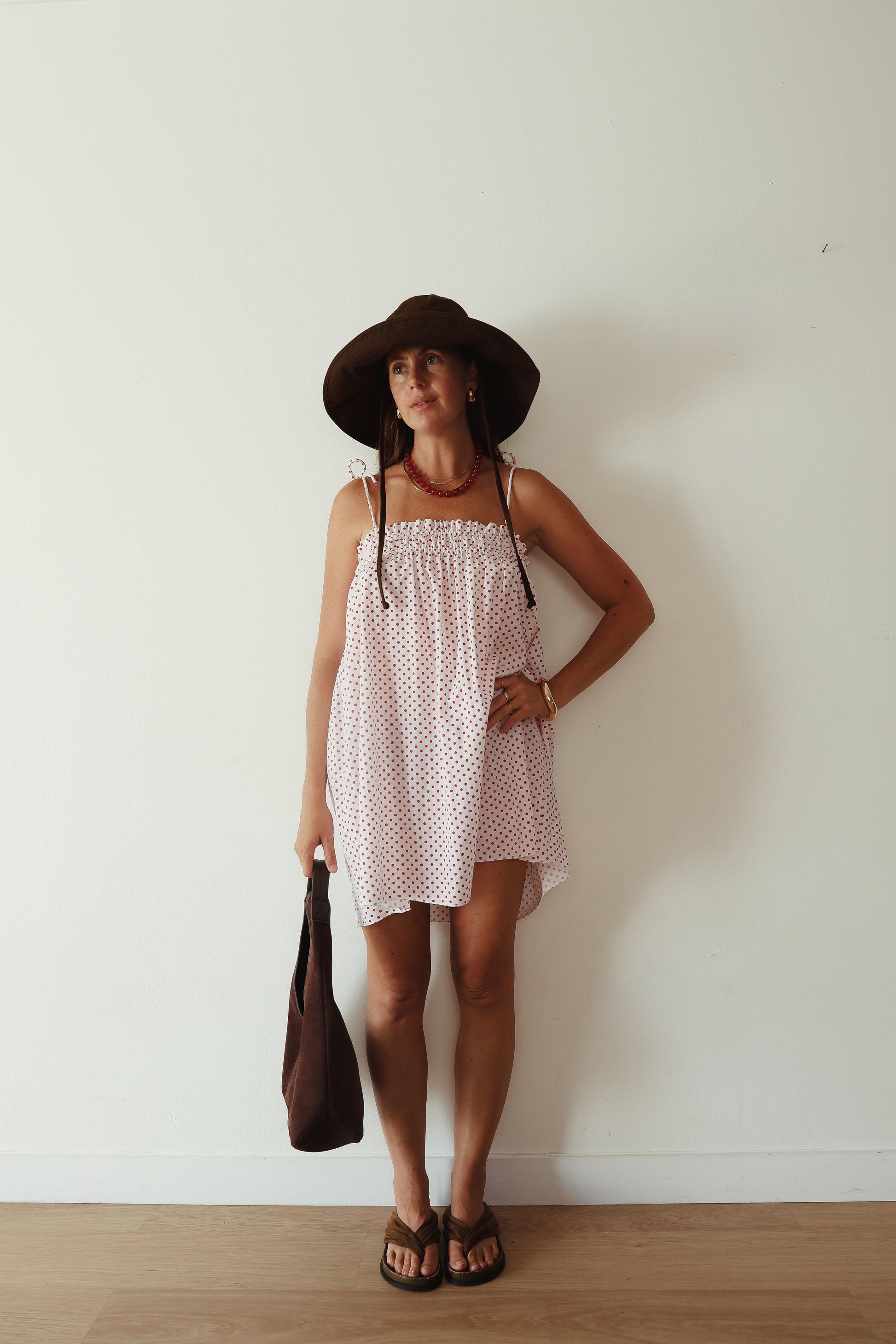 A white mini smock dress with a ruched bust and adjustable spagetti shoulder straps that tie. The fabric is 1a light weight 100% soft cotton in white with red polkadots.
