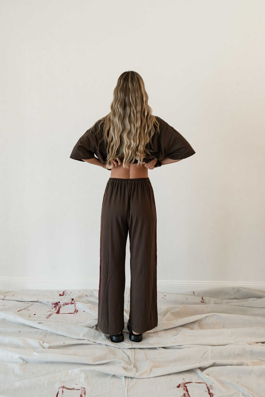 Model wears a two piece set in a rich chocolate brown organic cotton relaxed wide leg pant with side gold heart snap buttons down the leg with an oversized tshirt also in the rich chocolate brown organic cotton