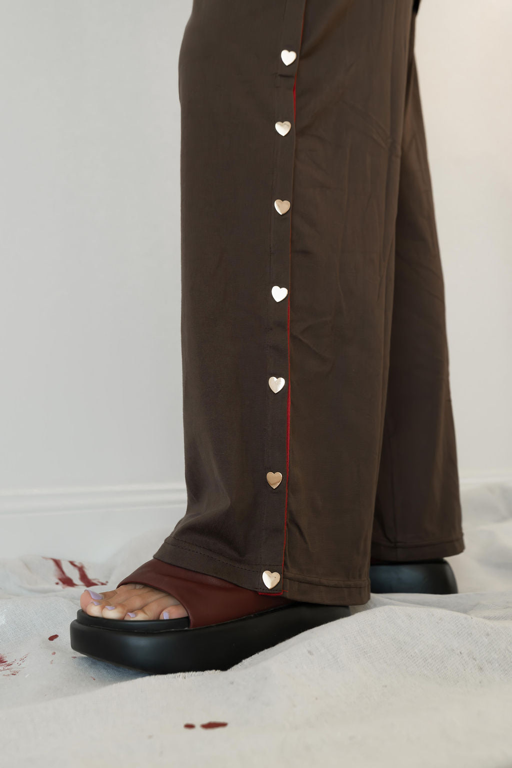 Model wears a two piece set in a rich chocolate brown organic cotton relaxed wide leg pant with side gold heart snap buttons down the leg with an oversized tshirt also in the rich chocolate brown organic cotton