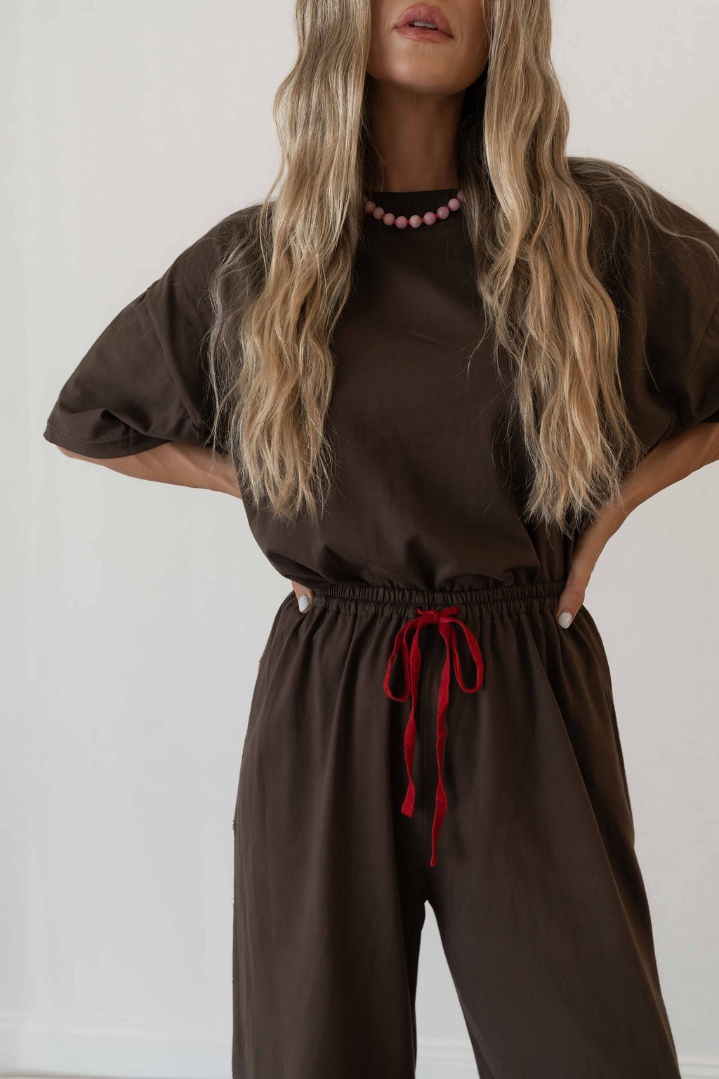 Model wears a two piece set in a rich chocolate brown organic cotton relaxed wide leg pant with side gold heart snap buttons down the leg with an oversized tshirt also in the rich chocolate brown organic cotton