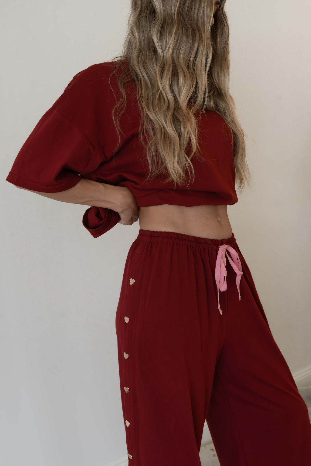 Model wears a two piece set in a deep merlot organic cotton relaxed wide leg pant with side gold heart snap buttons down the leg with an oversized tshirt also in the deep merlot red organic cotton