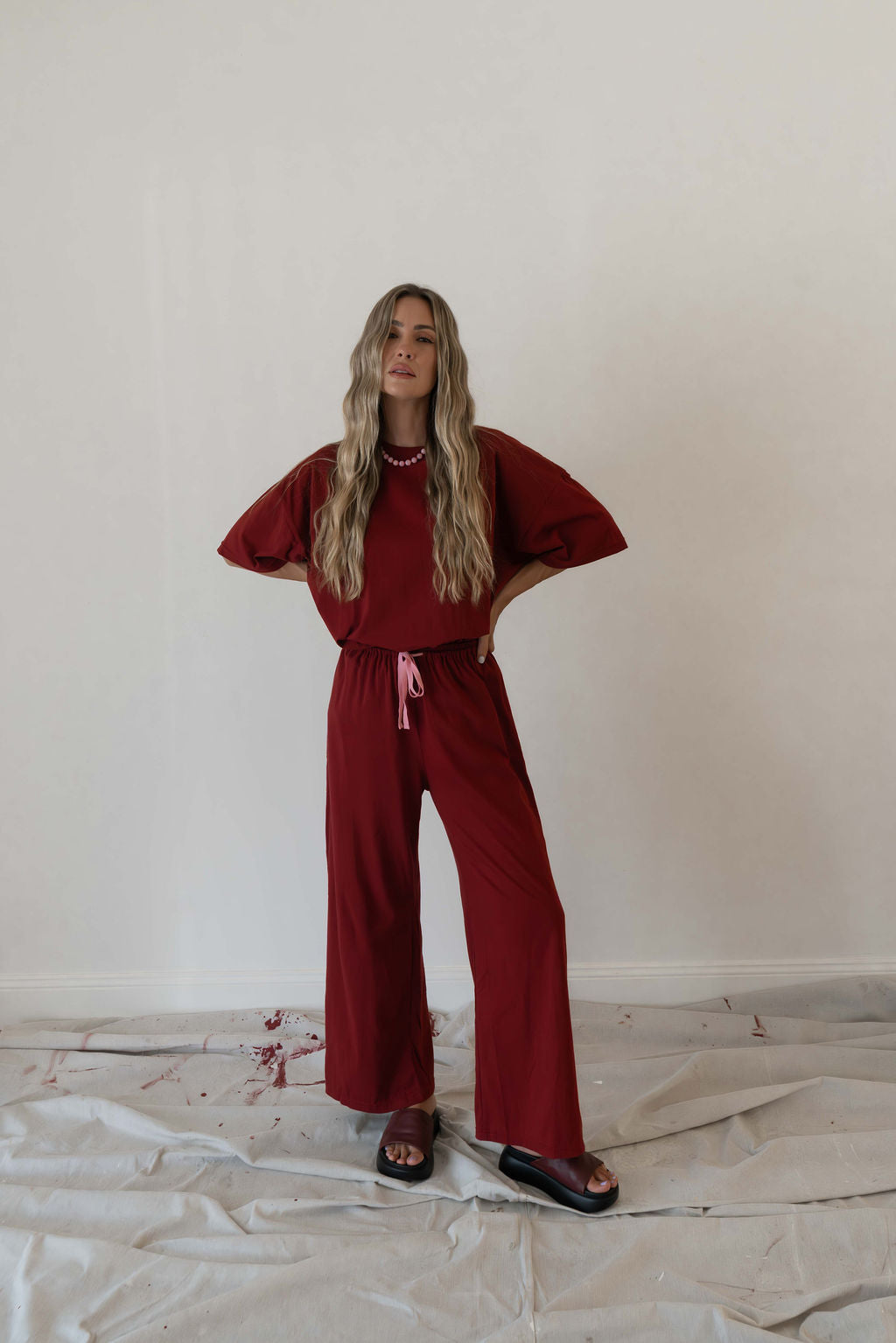 Model wears a two piece set in a deep merlot organic cotton relaxed wide leg pant with side gold heart snap buttons down the leg with an oversized tshirt also in the deep merlot red organic cotton
