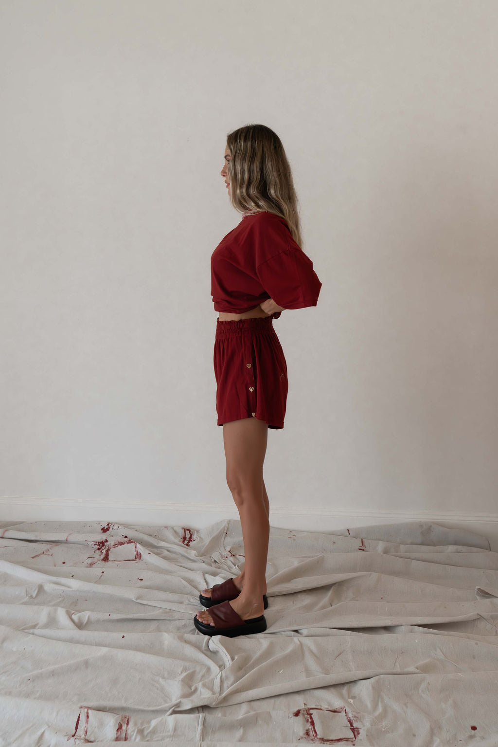 Model wears a two piece set in a deep merlot red organic cotton relaxed short with side gold heart snap buttons down the leg and a contrast red stripe down side with an oversized tshirt also in the deep merlot red organic cotton