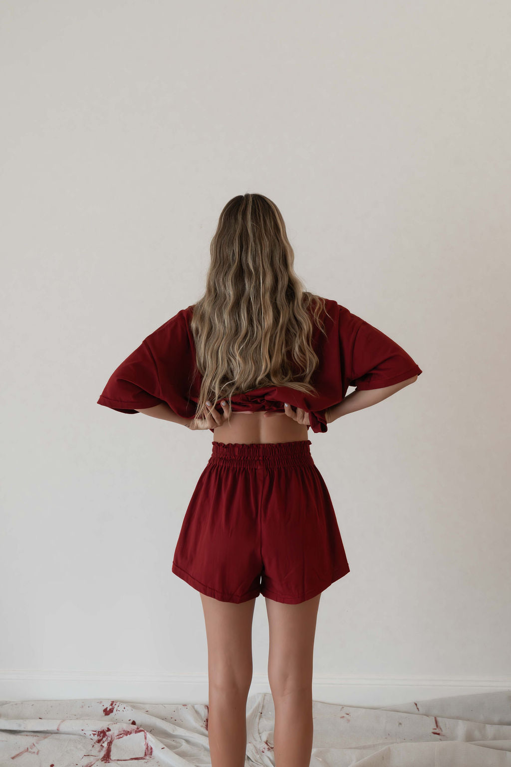 Model wears a two piece set in a deep merlot red organic cotton relaxed short with side gold heart snap buttons down the leg and a contrast red stripe down side with an oversized tshirt also in the deep merlot red organic cotton