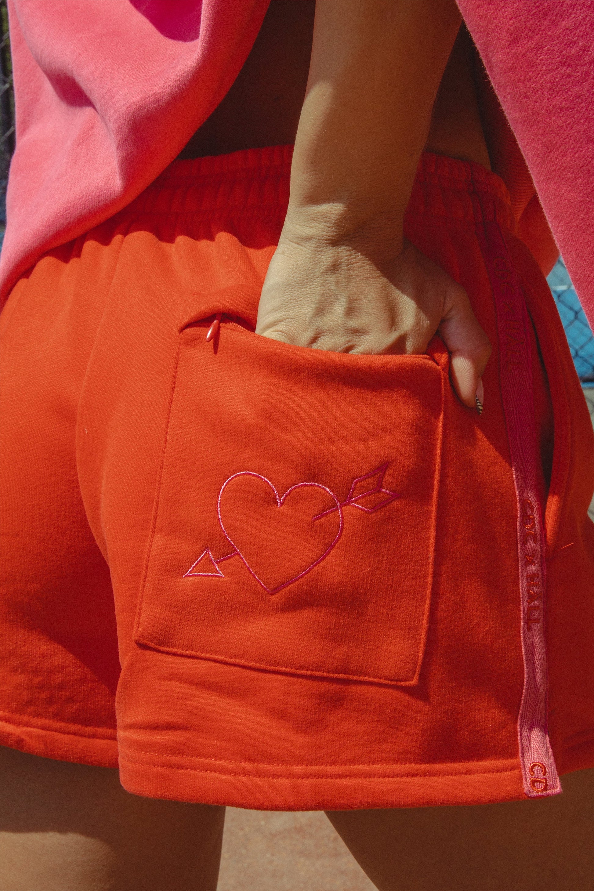 Red shorts with a heart design on the pocket held by a person wearing a pink sweater.