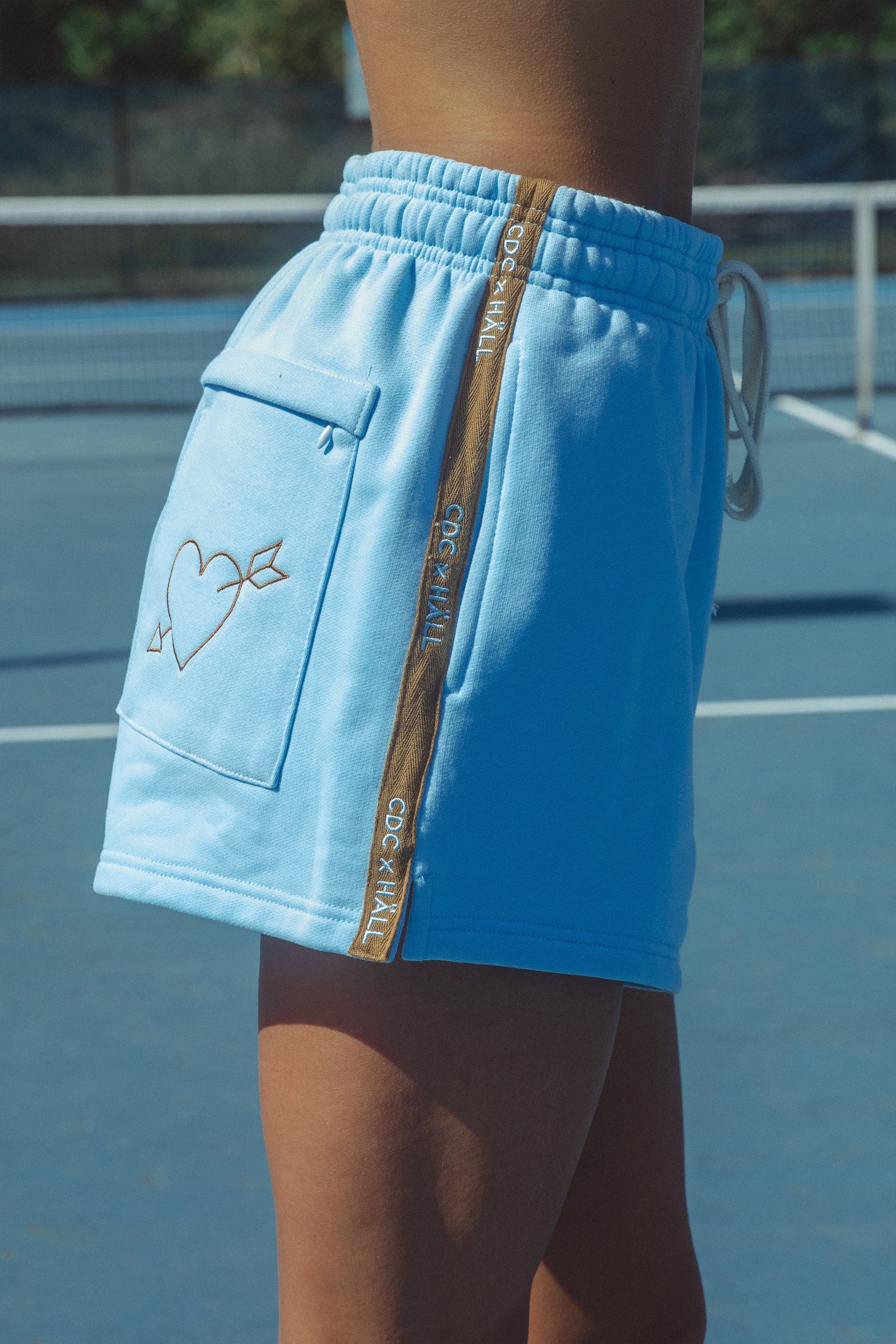 Blue shorts with embroidery and a cracker day club and hall store logo on a tennis court