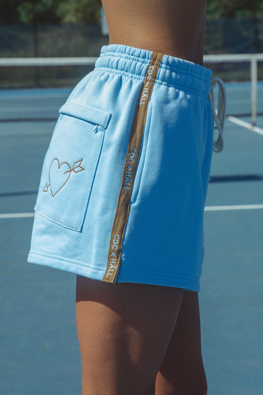 Blue shorts with embroidery and a cracker day club and hall store logo on a tennis court