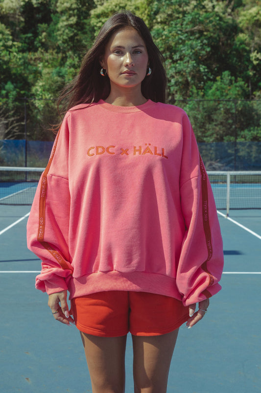 Woman wearing a pink sweatshirt with cracker day club x hall text on a tennis court