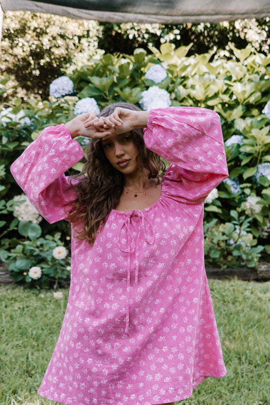 drawstring neckline shift mini dress with a statement balloon long sleeve with elastic wrists, rounded neckline with adjustable bow tie at the front. Hand painted white flower print on a bright candy pink cotton linen fabric.