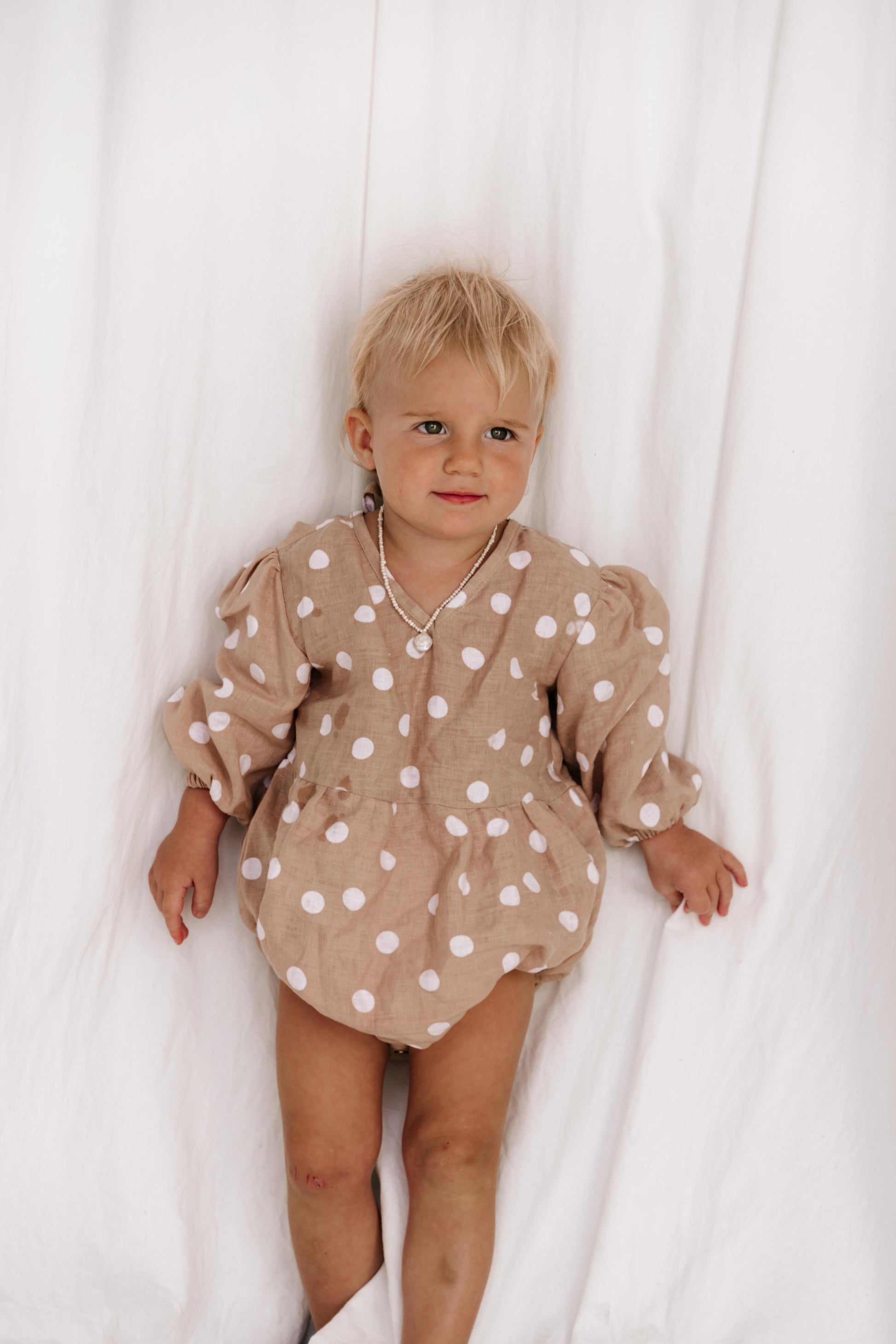 baby toddler romper in the cutest polkadot print nougat beige colour with white dots a v neck front a adjustable back with ties long sleeves with elastic cuffs