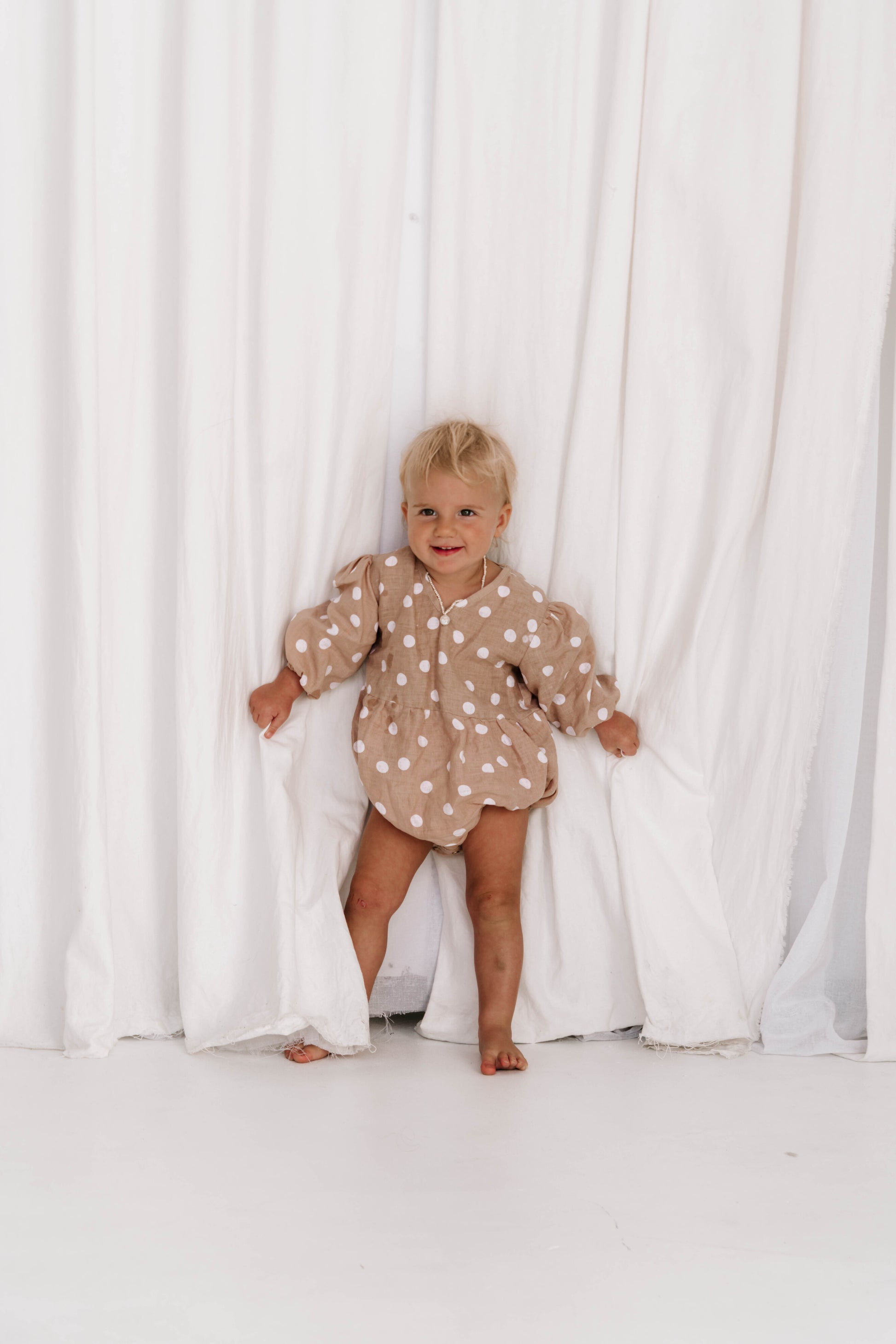 baby toddler romper in the cutest polkadot print nougat beige colour with white dots a v neck front a adjustable back with ties long sleeves with elastic cuffs