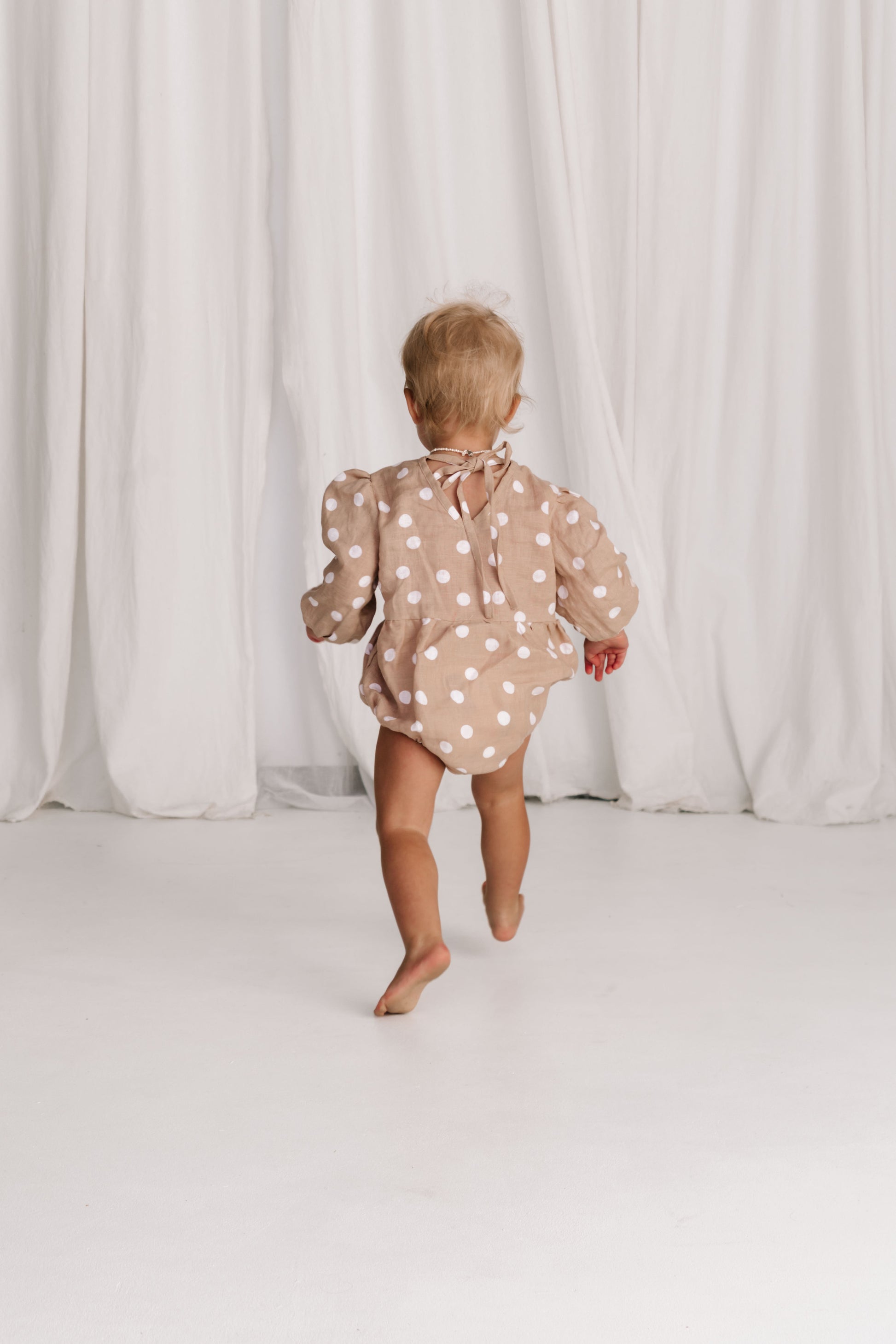 baby toddler romper in the cutest polkadot print nougat beige colour with white dots a v neck front a adjustable back with ties long sleeves with elastic cuffs