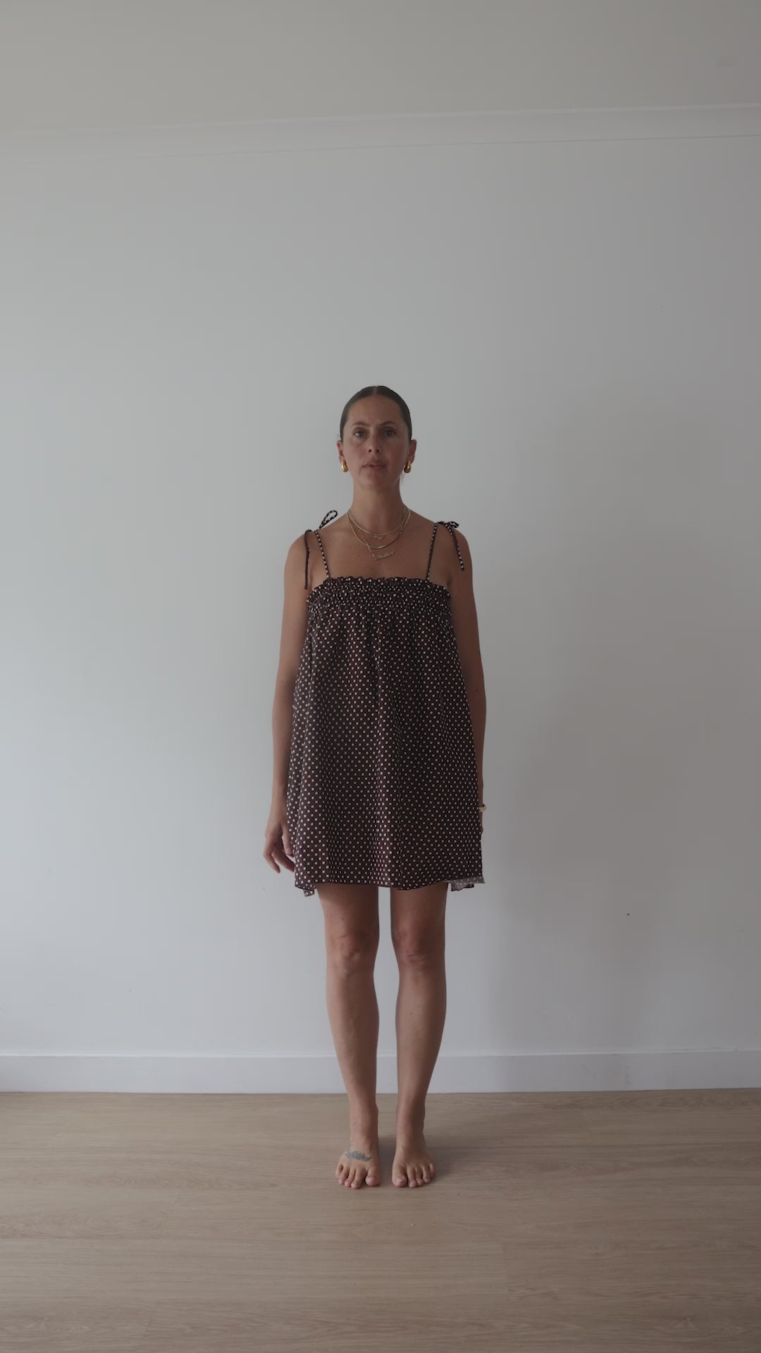 A chocolate brown mini smock dress with a ruched bust and adjustable spagetti shoulder straps that tie. The fabric is a light weight 100% soft cotton in butter yelllow with white lilac polkadots.
