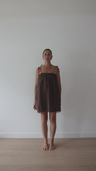 A chocolate brown mini smock dress with a ruched bust and adjustable spagetti shoulder straps that tie. The fabric is a light weight 100% soft cotton in butter yelllow with white lilac polkadots.