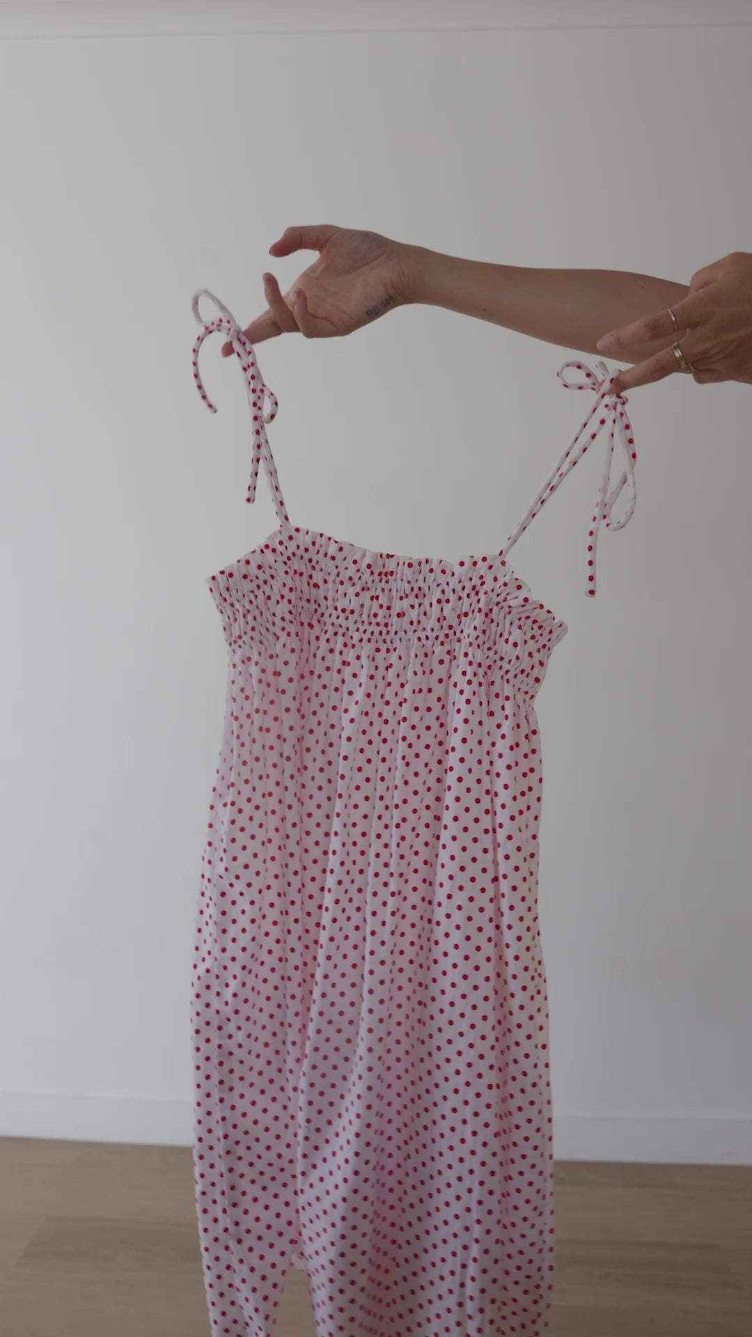A white mini smock dress with a ruched bust and adjustable spagetti shoulder straps that tie. The fabric is 1a light weight 100% soft cotton in white with red polkadots.